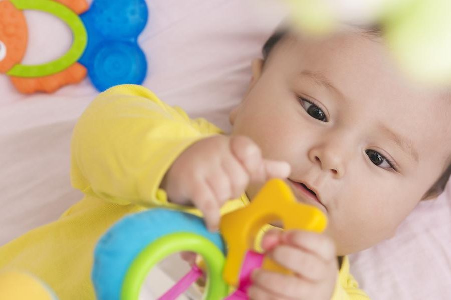 Happy baby lying in his crib looking at toy in his hands intently